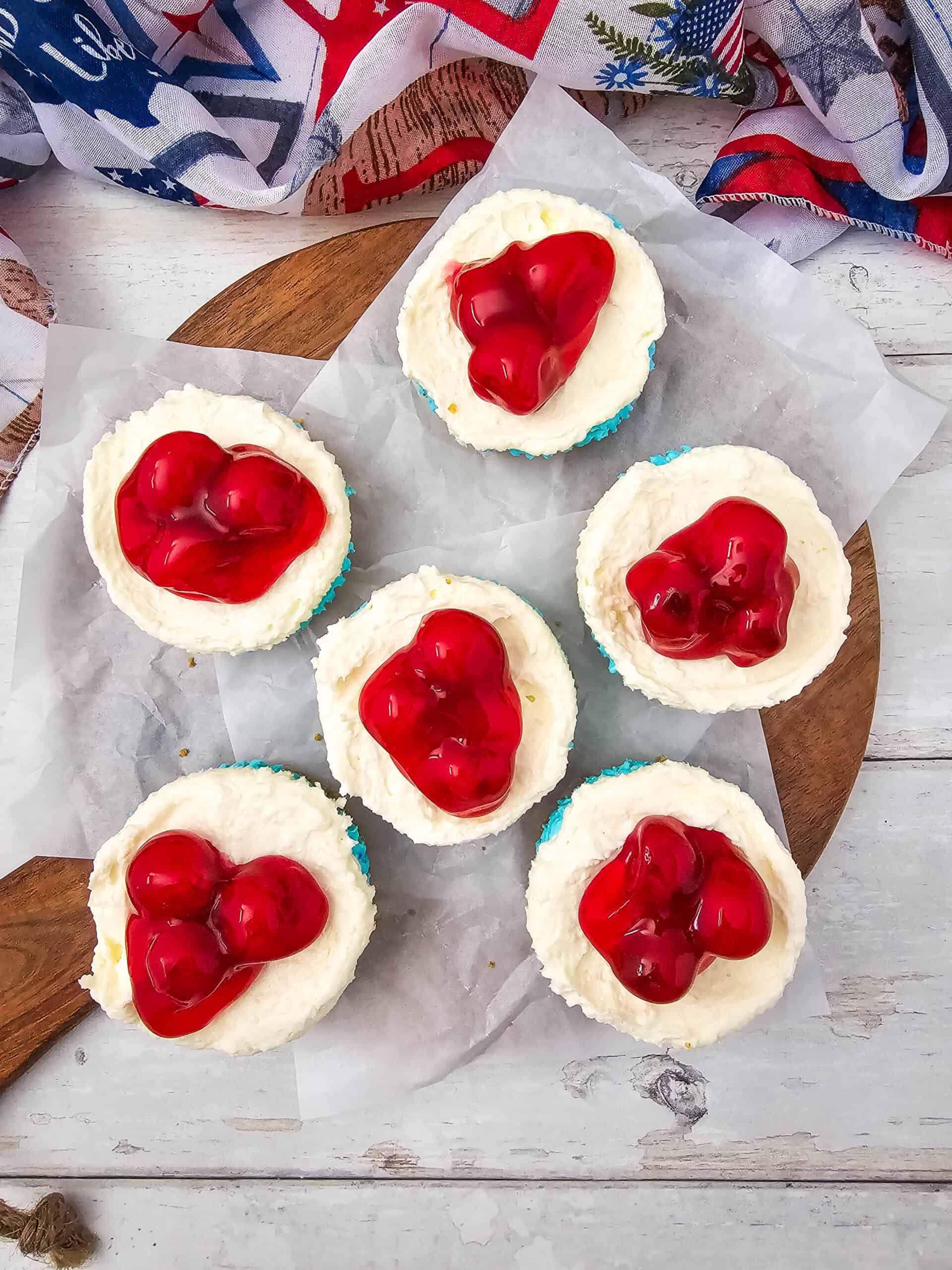 Festive no-bake Red, White, and Blue Cheesecake Bites with creamy blue and white cheesecake layers on a graham cracker crust, topped with bright red cherry pie filling.
