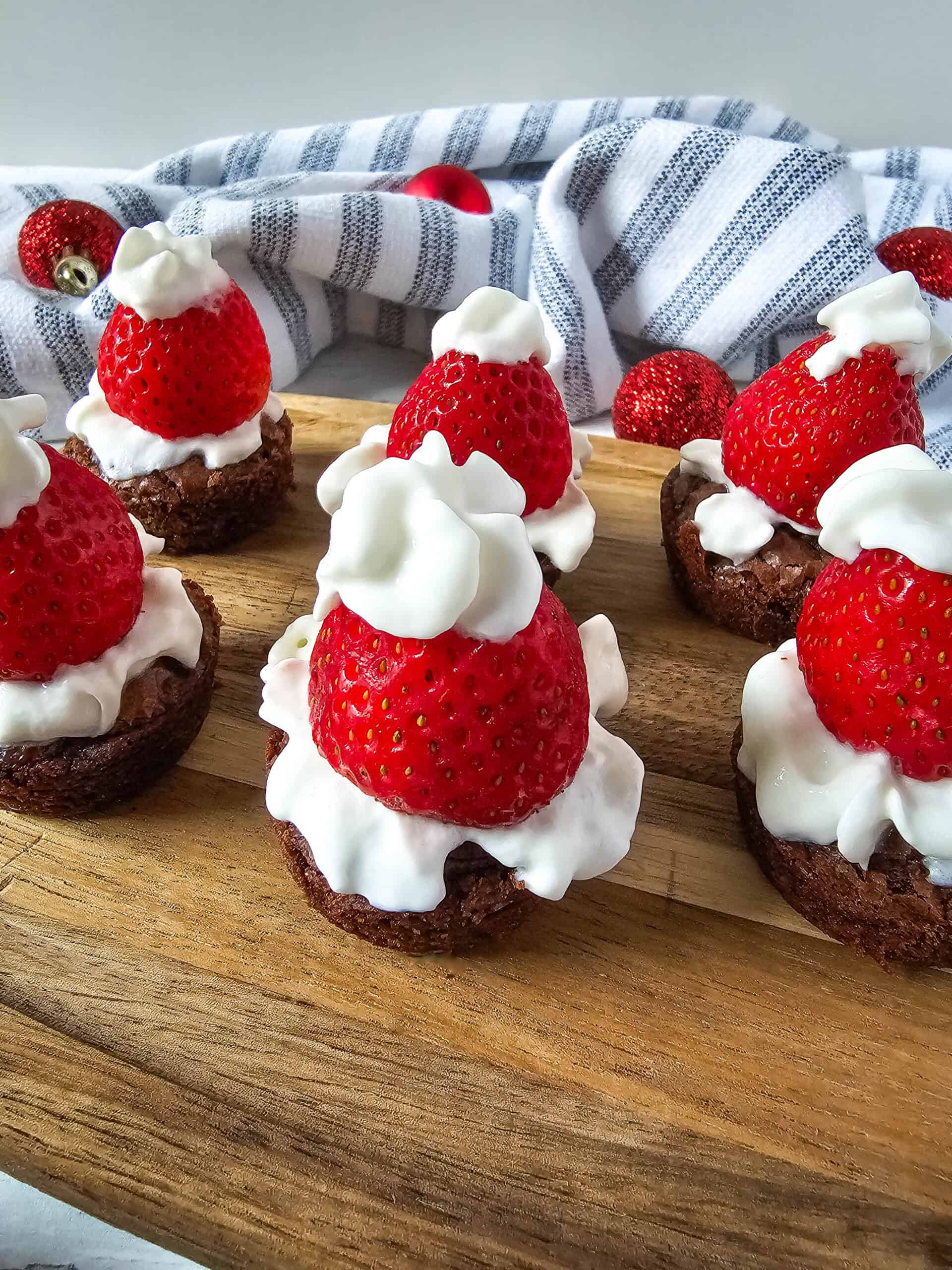 Festive Santa Hat Brownie Bites recipe with strawberries and whipped cream.