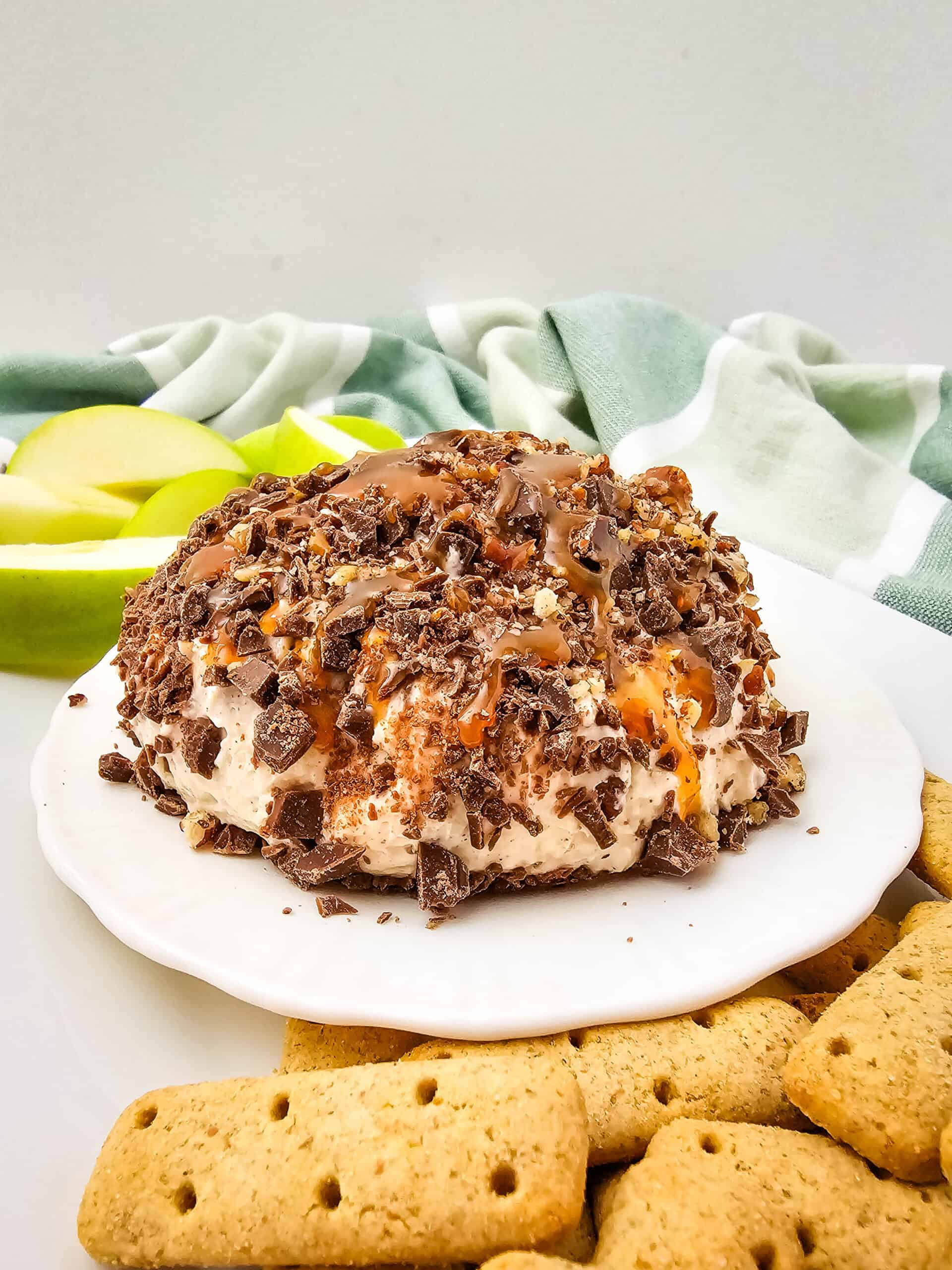 Caramel apple cheeseball recipe with cream cheese, caramel drizzle, pecans, and chocolate, served with apple slices.